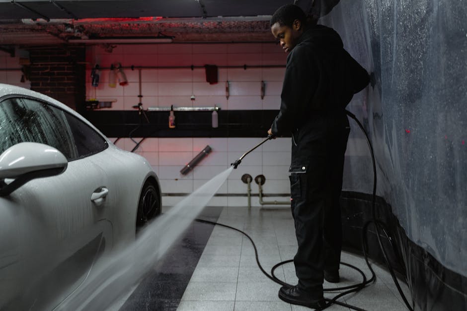 African American man cleaning a white car with a pressure hose in an indoor garage setting.
