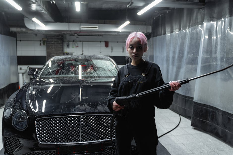 Person using a pressure washer to clean a luxury black car in an indoor garage.