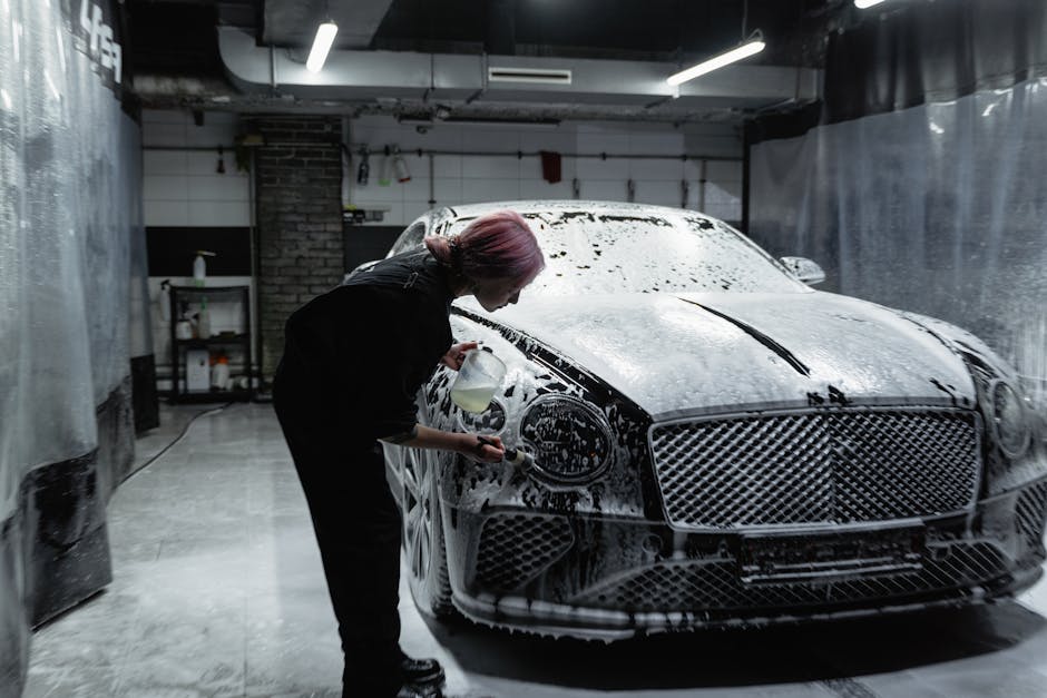 A worker professionally washing a luxury car in a modern garage filled with foam.